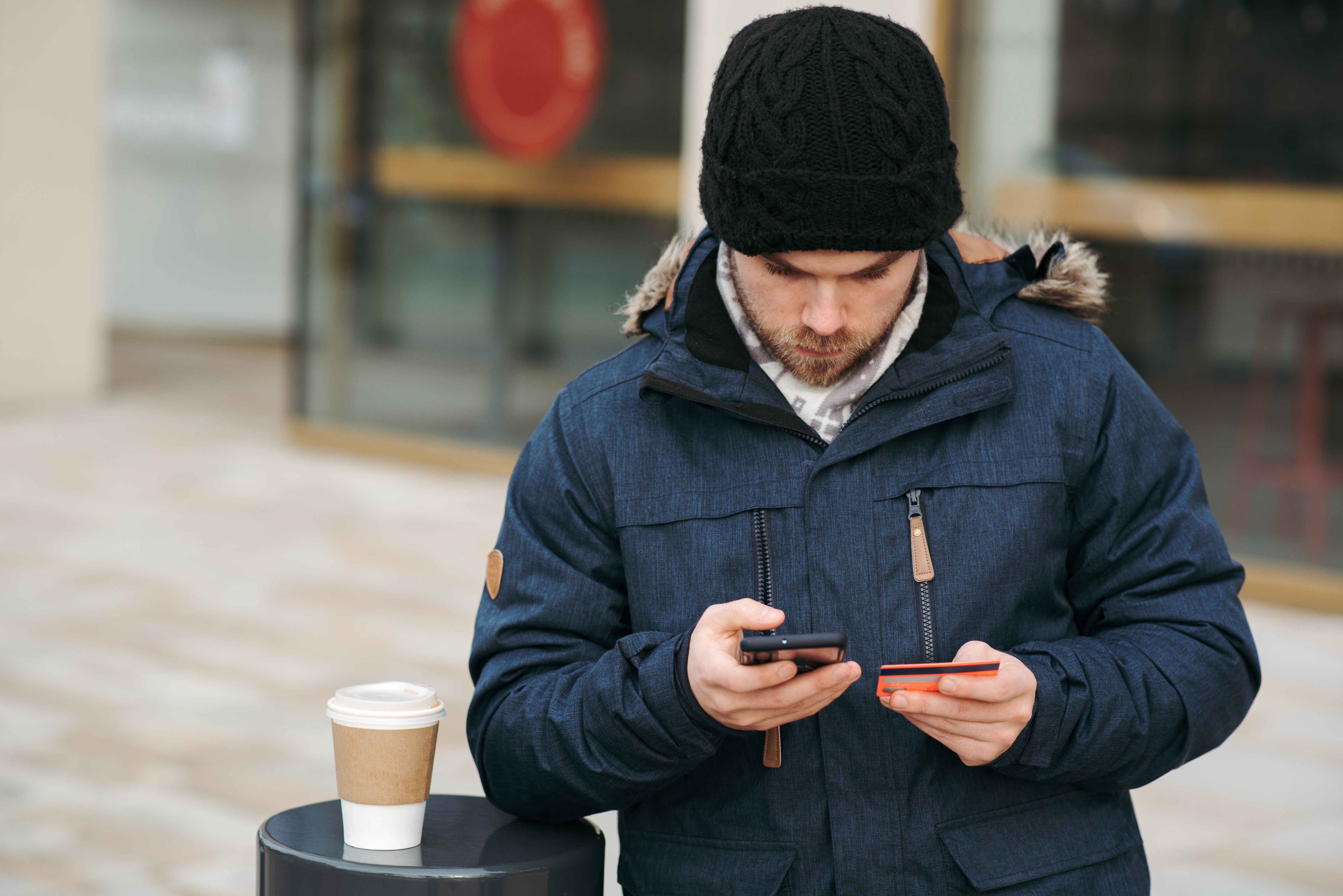 Focused male holding credit card while making payment with smartphone on street